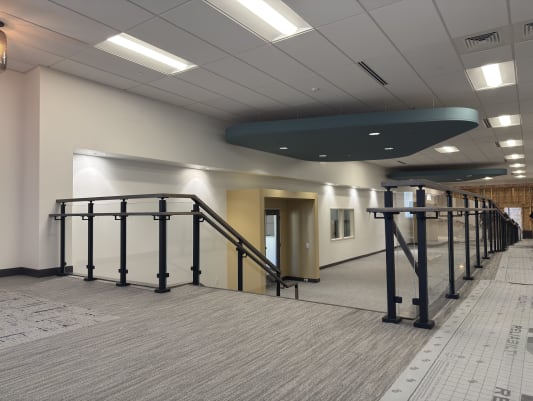 Black-post glass guardrail with handrails along a corridor stair and ramp