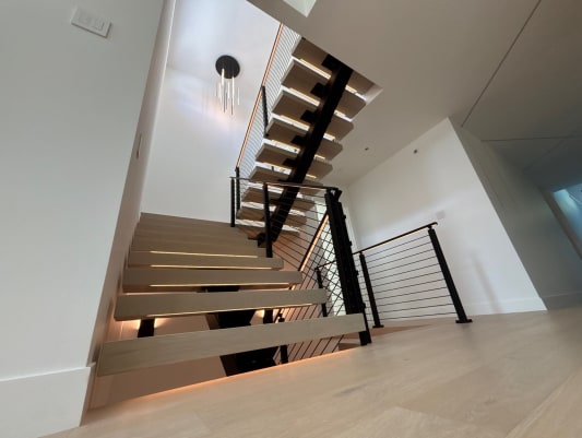 White oak floating treads with LED lighting and black cable railing rising to the upper floor