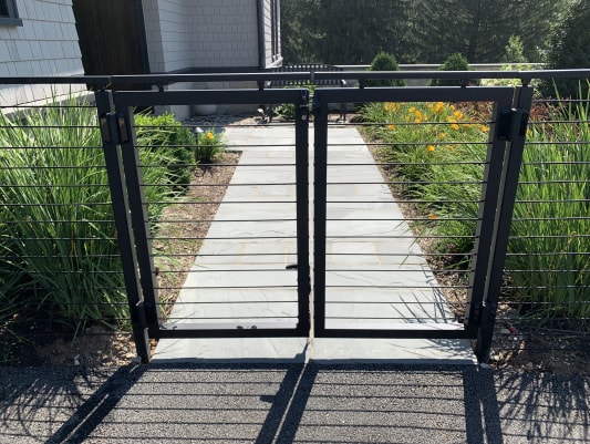 Black aluminum double gate with cable infill opening onto a bluestone garden path
