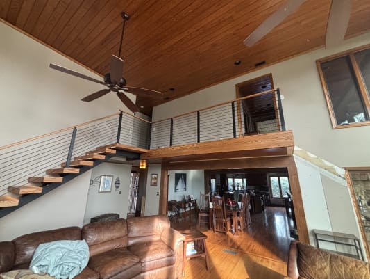 Pine floating treads on a black mono stringer with black cable railing and pine handrail rising to a loft under a tongue-and-groove ceiling