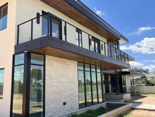 Black cable railing wraps a second-story balcony above a stone and glass modern facade.
