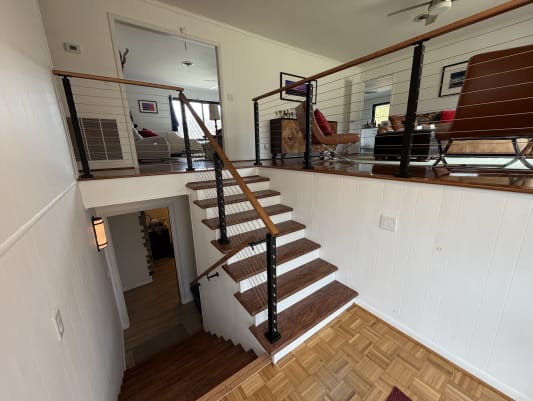 Black cable railing posts with a warm wood handrail line a split-level stair with white risers and cherry-toned treads.