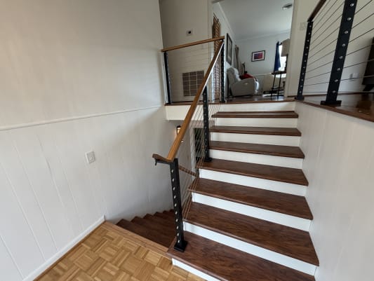 Black cable railing posts with a warm wood handrail line a split-level stair with white risers and cherry-toned treads.