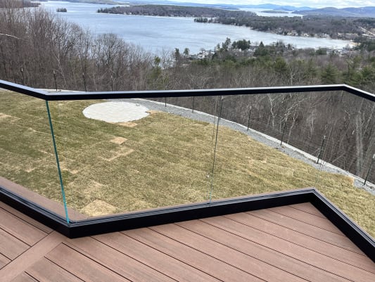 Frameless glass in a black base channel with black cap follows an angled deck edge with a wide lake view.