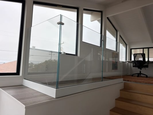 A frameless glass corner guard edges a loft landing in front of large black-framed windows.