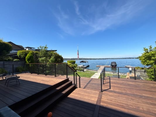 Hardwood deck levels with steps are bordered by black cable railing leading toward a lake and boat dock.
