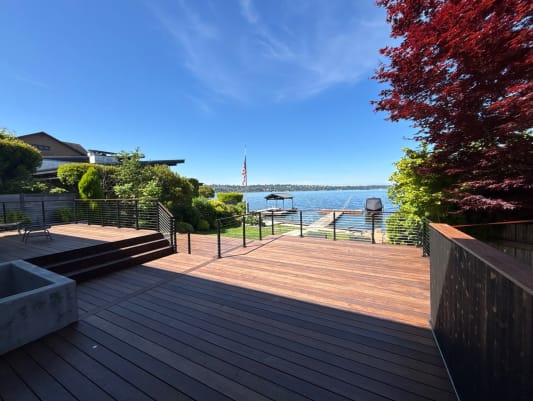 Steps join tiered hardwood decks lined with black cable railing beneath a red maple near the lake.