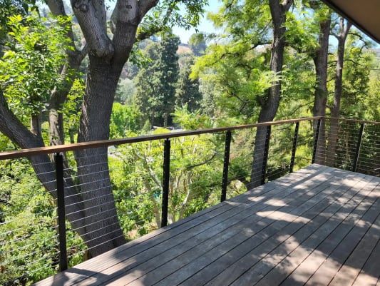 A wood-capped black cable railing edges a shaded hardwood deck overlooking wooded hills.