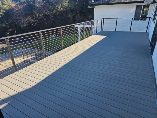 Side-mount Express cable railing surrounds a wide composite deck on a white home.