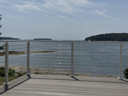 White cable railing frames a composite deck overlooking a calm bay with wooded islands.