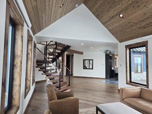 A black FLIGHT switchback with walnut treads and cable railing under a cedar ceiling in an open living room.