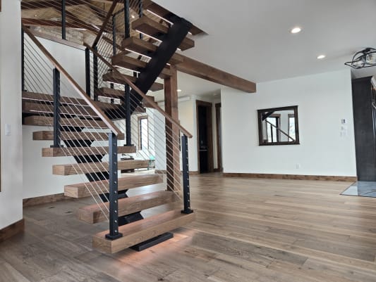 Thick walnut treads on a black FLIGHT switchback with cable railing rise from an LED-lit plinth.