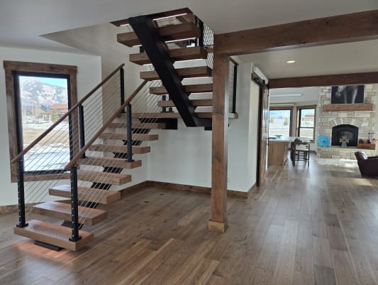 A black FLIGHT switchback with walnut treads, cable railing and LED base beside a timber post and mountain-view windows.