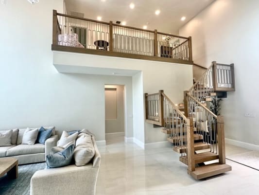 A mono stringer stair with wood and metal railing rises to a balustraded loft above a bright living room.