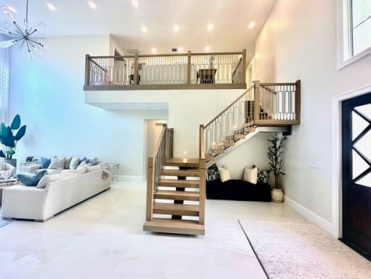 Oak floating treads with a wood and metal railing lead up to a matching loft balustrade above a white living area.