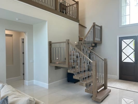 Oak mono stair with wood newels and geometric balusters turns at a landing next to a dark front door.