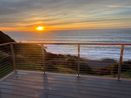 Horizontal rod railing with wood cap frames a sunset over the ocean from a composite deck.