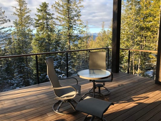 Black rod railing with wooden cap around an ipe deck with patio chairs overlooking a forested valley.