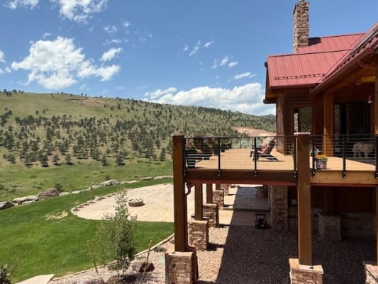 Elevated wood deck with black cable railing on a mountain home overlooking green foothills.