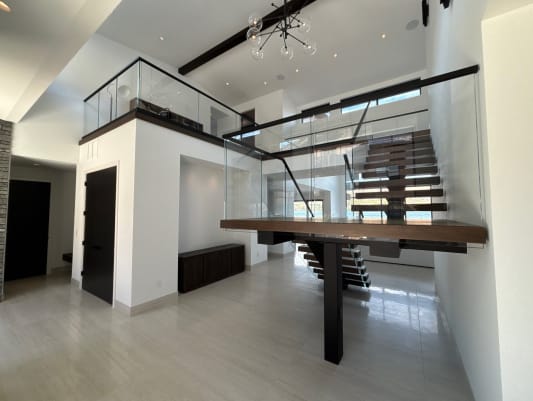 Dark wood floating treads on a black mono stringer switch back at a wood landing, framed by frameless glass on base rail in a bright double-height entry.