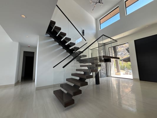 Dark wood floating treads with frameless glass and black handrail switch back at a landing beneath clerestory windows.