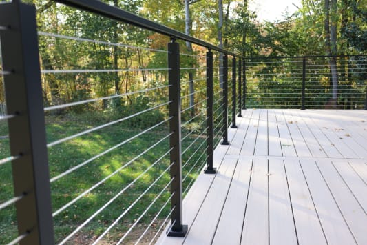 A long black cable railing runs along a light composite deck amid autumn woods.