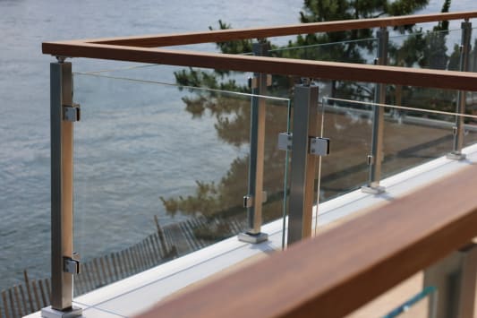 Stainless posts with glass clamps and a hardwood top rail edge a balcony above the water.