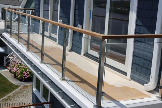 Stainless posts with glass infill and hardwood cap line a balcony on a blue-shingled coastal house.