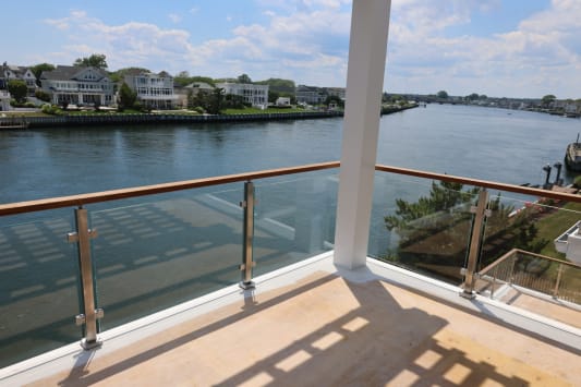 Stainless posts and a hardwood top rail frame glass panels on a balcony overlooking a calm residential waterway.