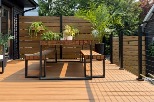 Composite deck with a wood-and-metal dining set, potted palms and black-post cable railing along the edge.