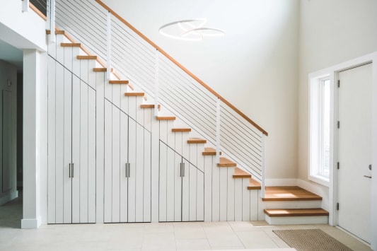 White posts with horizontal cable and a wood handrail run along a white stair with built-in storage.