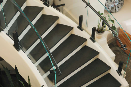 Overhead view of curved glass railing on black talons and a dark handrail along a white curved stair.