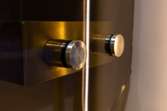 Close-up of brushed stainless standoff pins holding glass to a dark wood fascia.