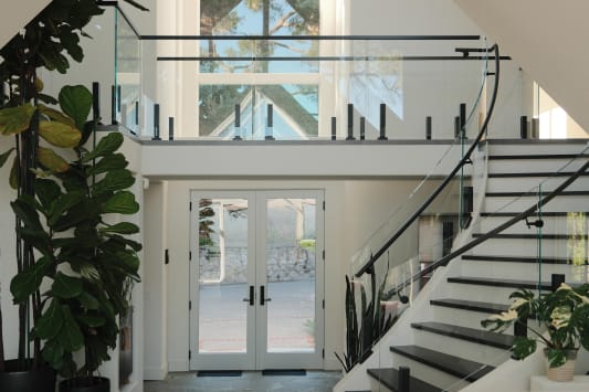 Frameless glass on black Ascend Talons with a curved black handrail follows a sweeping white stair up to a glass-railed gallery.