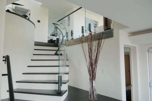 Black talon-clamped glass panels curve along a white stair with dark treads in a bright modern entry.