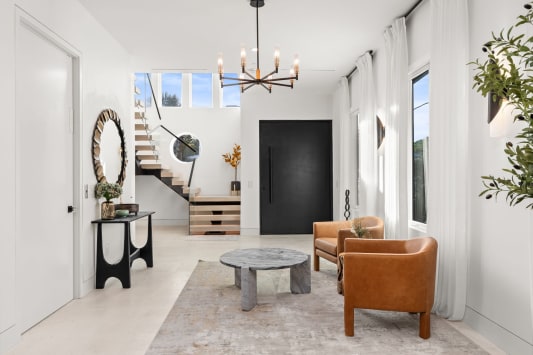 Styled white foyer with a floating stair and glass guard rising to a landing behind the seating area.