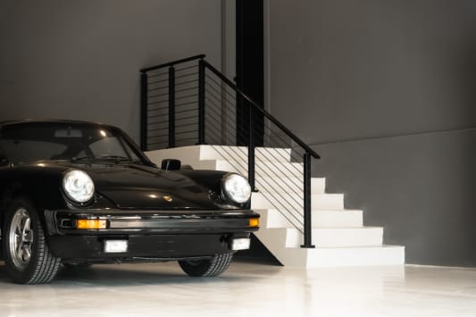 White stair in a gray showroom garage with black horizontal rod railing behind a classic black sports car.