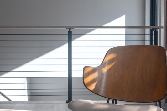 Black horizontal rod railing with wood cap in a sunlit room beside a molded wood chair.