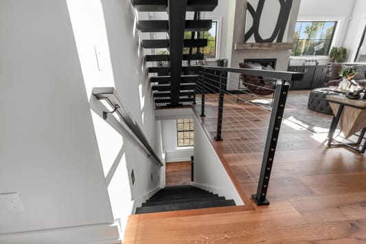 Black cable railing guards a stair opening beside a wall handrail, with a floating stair rising above.