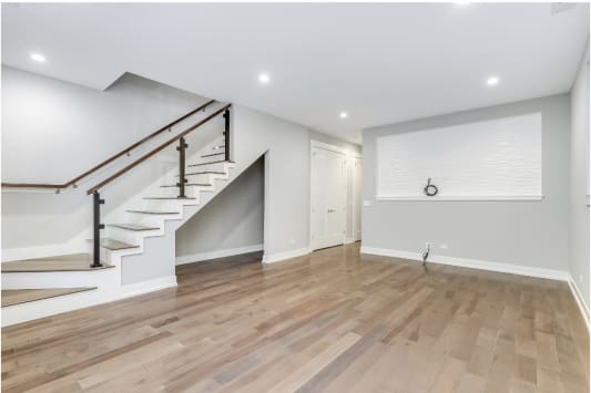 Black posts with glass panels and a wood handrail along a white stair in a finished basement.