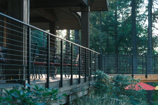 Black cable railing wraps an elevated deck and covered porch among firs and rhododendrons.