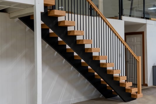 Long run of oak floating treads on a black stringer with slim black balusters and an oak handrail rising to a loft.