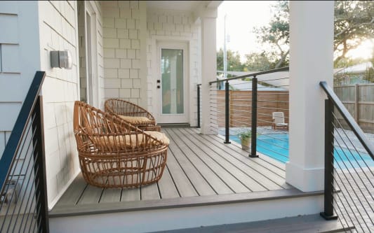 Black horizontal rod railing along a composite deck beside a backyard pool, with wicker chairs.