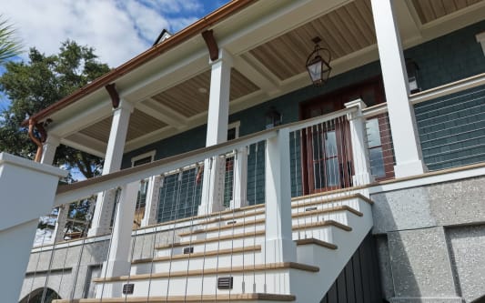 Wide front porch stair on a coastal home with white posts, wood handrail and vertical cable infill.