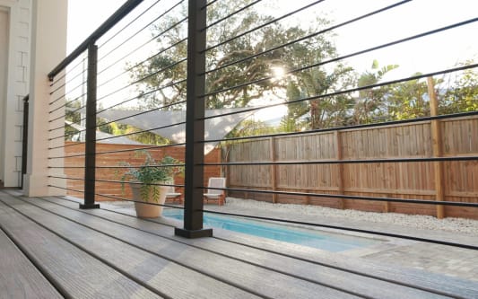 Low-angle view of black rod railing along a gray composite deck beside a narrow plunge pool.