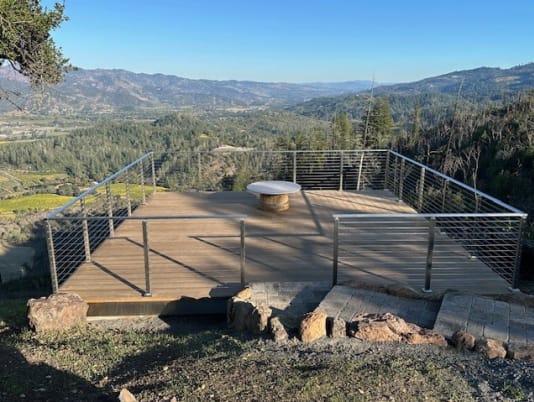 Brushed stainless cable railing framing a wood deck with stone steps above a vineyard valley.
