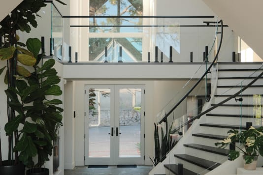 Frameless glass on black Ascend Talons with a curved black handrail follows a sweeping white stair up to a glass-railed gallery.