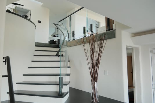 Black talon-clamped glass panels curve along a white stair with dark treads in a bright modern entry.