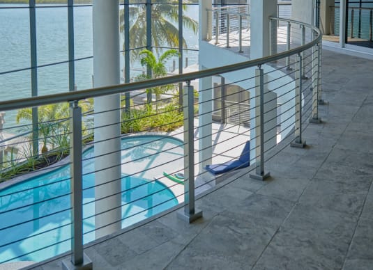 A sweeping curved stainless cable railing lines a stone terrace above a pool with palms and water beyond.