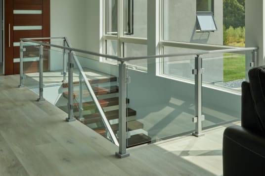 Silver post-to-post glass railing surrounds a floating stair opening beside tall windows.